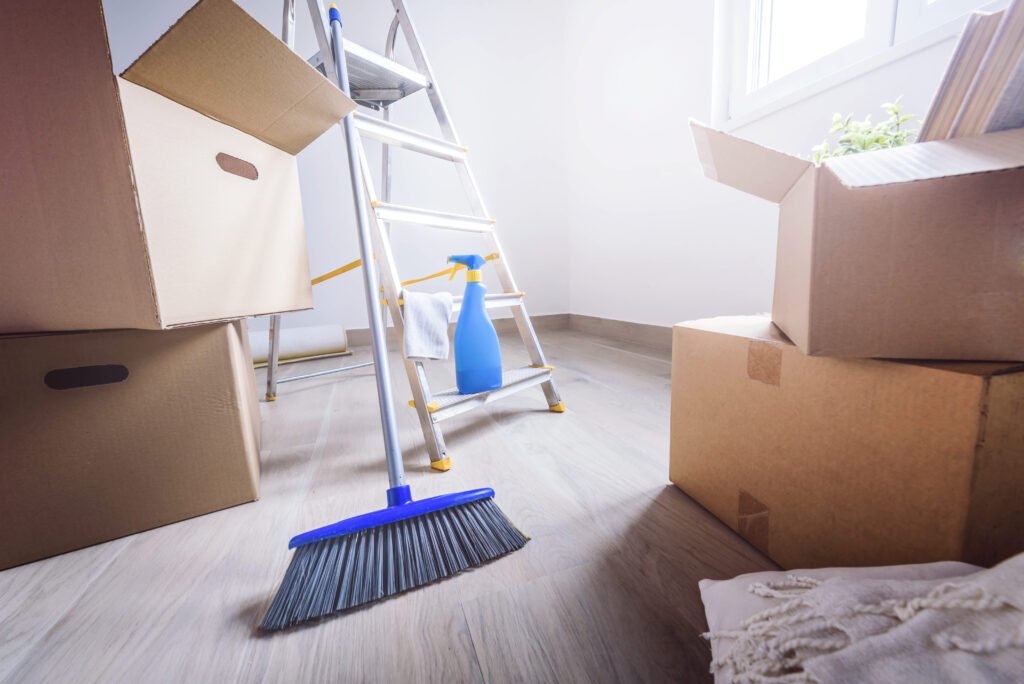 A broom, spray bottle, and ladder surrounded by moving boxes, highlighting the choice between Recurring Cleaning vs One Time Deep Cleaning for new or transforming spaces