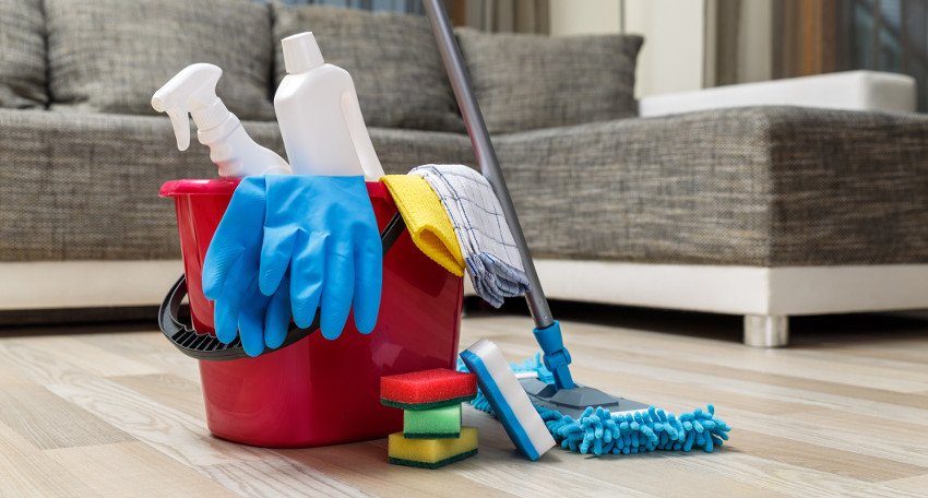 A bucket filled with cleaning supplies sits on a wooden floor, ready for weekly cleaning tasks.